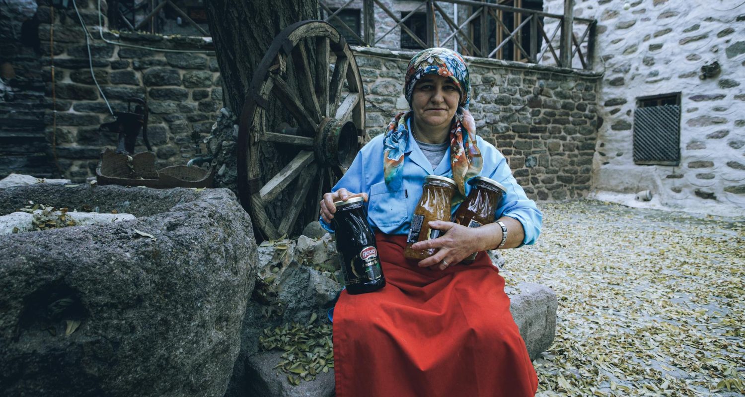 Mujer artesana en su pequeño negocio en un pueblo rural, trabajando con sus manos en una pieza tradicional, rodeada de materiales y herramientas que reflejan su historia y herencia cultural.